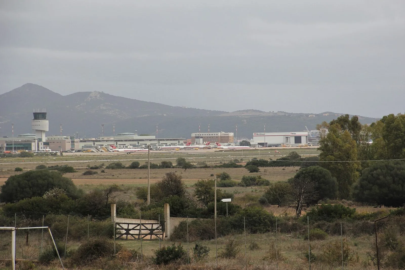 L'aeroporto di Olbia Costa Smeralda visto da lontano, con la torre di controllo, gli aerei sul piazzale e le colline sullo sfondo