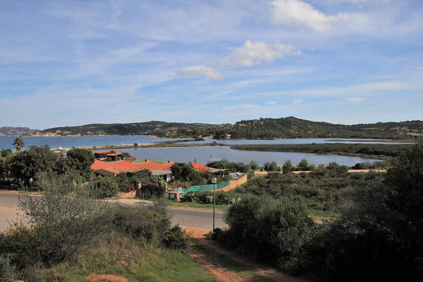 Lo stagno di Porto Taverna separato dal mare da una lingua di sabbia, con le colline coperte di macchia e il cielo velato