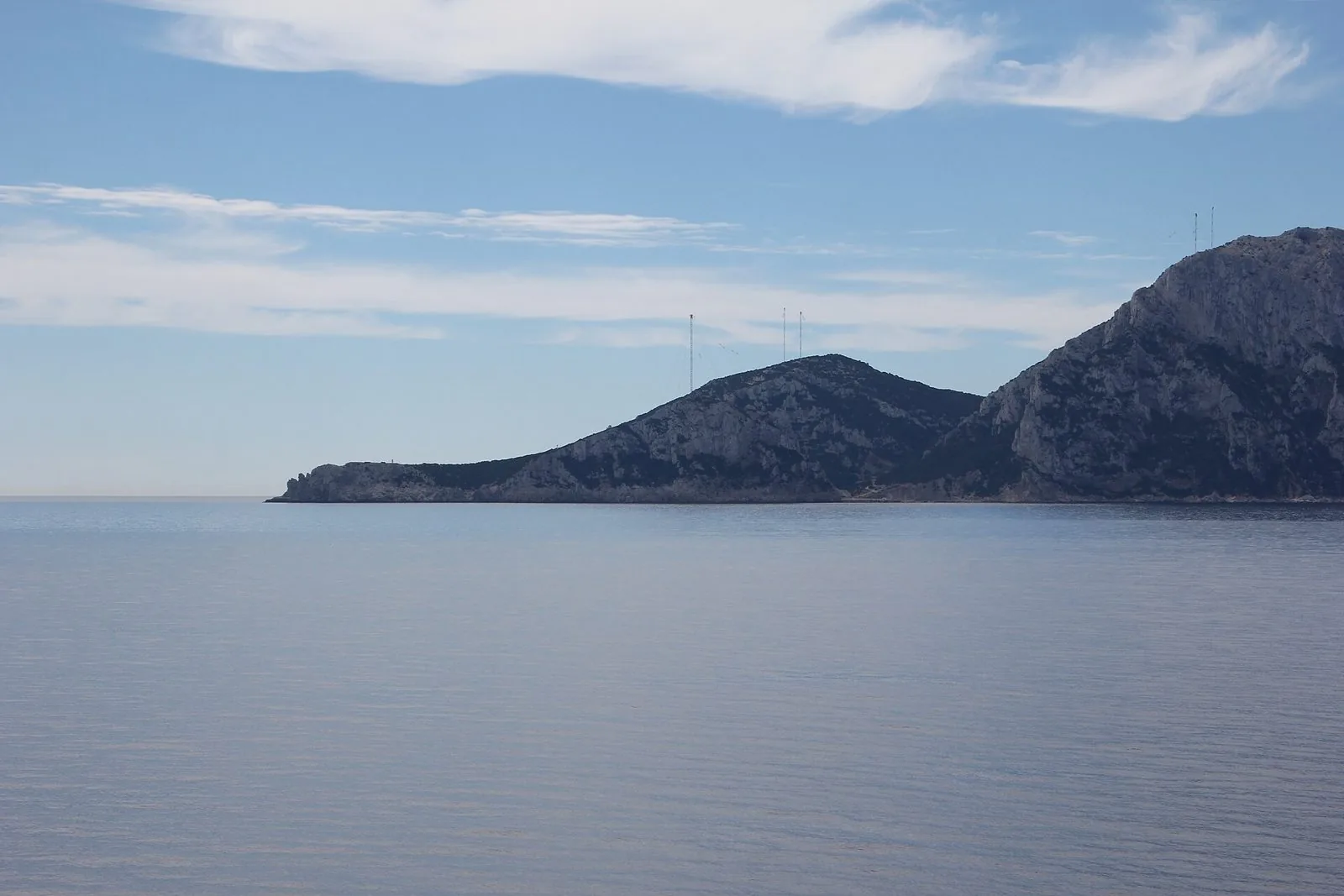 Il profilo roccioso dell'isola di Tavolara sul mare calmo, con alcune antenne sulle alture del promontorio