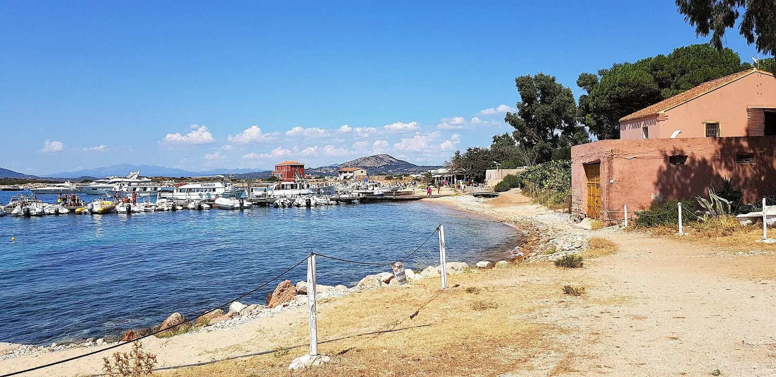 Il pontile dello Spalmatore di Terra a Tavolara con barche ormeggiate, una piccola baia e una casa rosa tra i pini